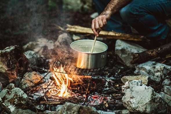 Photo of a man stirring a campfire cooking pot by Gary Sandoz